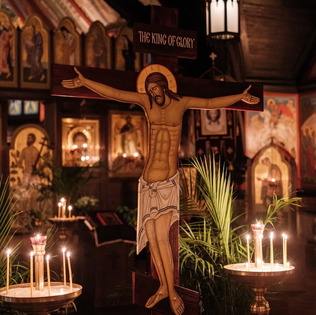 A carved crucifix flanked by candle stands and palm fronds, beneath an icon-covered wall